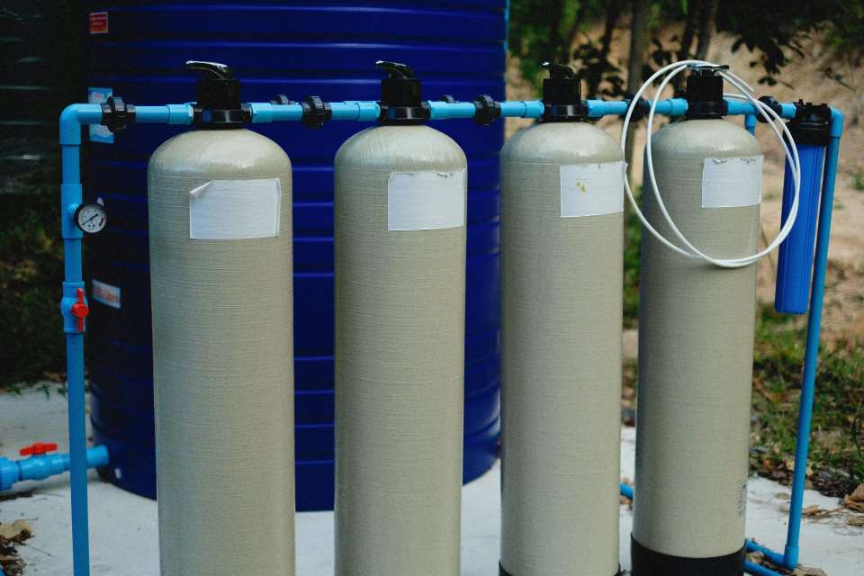 Vier beige Tanks in einer Wasseraufbereitungsanlage im Freien mit blauen Rohrleitungen.